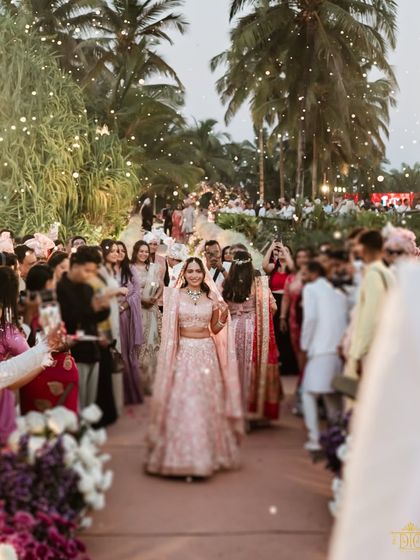 The bride's grand entrance down an aisle lined with her loved ones. The outdoor setting with palm trees and soft lighting was designed to create a beautiful and emotional start to the wedding ceremony.