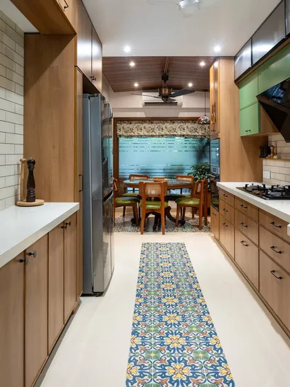 This galley kitchen was designed for a seamless flow into the dining area. The warm wood cabinets and patterned floor runner create a continuous visual path, making the two distinct spaces feel like one harmonious whole.