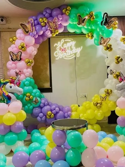 A magical unicorn and butterfly themed birthday party. The setup includes a circular balloon arch in rainbow colors, unicorn foils, and a 'Happy Birthday' neon sign.