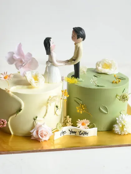 This unique two-part cake was designed to celebrate an anniversary for a couple living in different countries. The separate cakes, in cream and sage green, are united by a custom topper and delicate florals, symbolizing their strong bond.