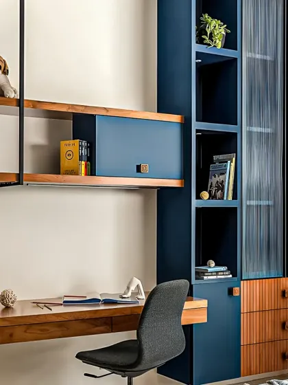Functionality is key in our designs. This integrated study and storage unit features a floating desk, fluted glass cabinetry, and a mix of open and closed shelving in a modern blue and wood finish.