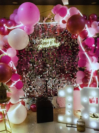 A glamorous 18th birthday setup with a pink shimmer wall, a pink and white balloon arch, and large marquee numbers.