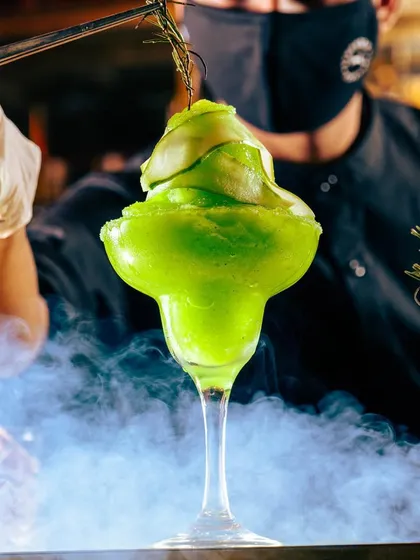 A close-up of our vibrant green frozen cocktail. The smoky presentation and fresh garnish highlight our commitment to creating an extraordinary and memorable beverage experience.