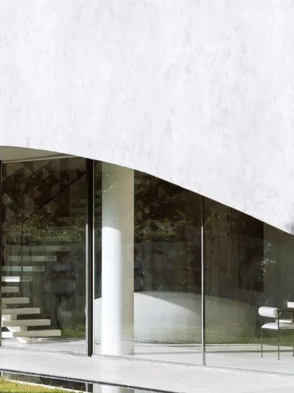 The minimalist glass facade of Villa KD 45, which allows for uninterrupted views of the garden. The floating staircase inside is visible, adding a touch of sculptural elegance to the interior.