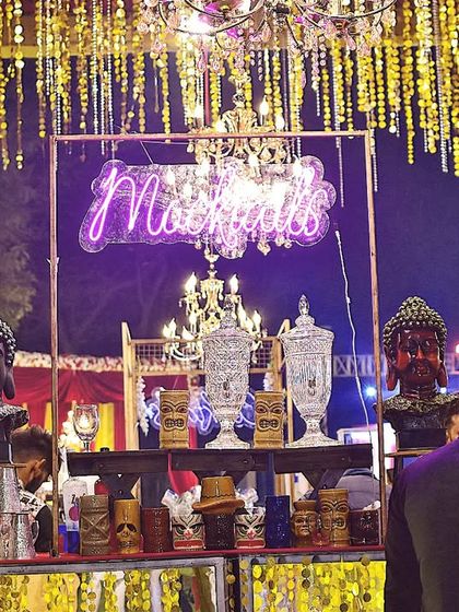 This is a luxury bar setup designed for a grand wedding reception. Featuring multiple crystal chandeliers, a 'Mocktails' neon sign, and ornate decor, it exudes opulence and sophistication.