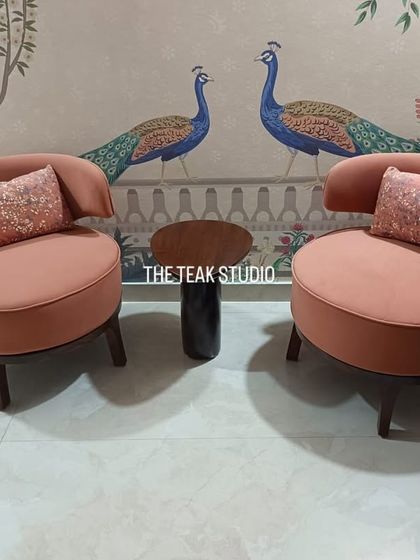 Another view of these charming dusty pink accent chairs, shown here in a beautifully styled setting against a wall with peacock murals. The chairs' soft curves and warm color create a welcoming and artistic atmosphere.