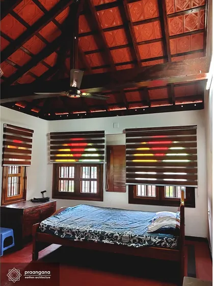 A bedroom in the Udupi house, featuring a high ceiling with exposed wooden rafters and Mangalore tiles. This design promotes air circulation, keeping the room naturally cool.