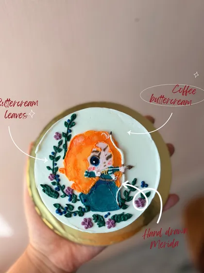 Your favorite characters can become edible art. Here, I hand-drew Merida from 'Brave' using colored buttercream, adding delicate buttercream leaves and flowers to frame the design on this coffee-flavored bento cake.
