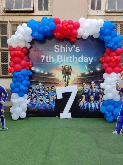 A sports-lover's dream party combining cricket and football themes. This outdoor setup features a custom backdrop, a red, white, and blue balloon arch, and life-sized cutouts for fun photo opportunities.