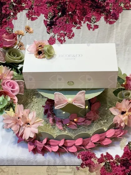 A circular gift tray decorated in shades of pink and green. This hamper, featuring a luxury gift box from Jacob & Co, is surrounded by a wreath of handmade paper flowers, showcasing my attention to detail.
