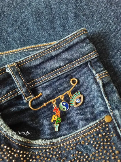 Your jeans and jackets deserve a glow-up too. These decorative safety pin charms are a super fun way to express your mood. This one features a 'HAPPY' charm, a yin-yang for balance, and an evil eye for good vibes.