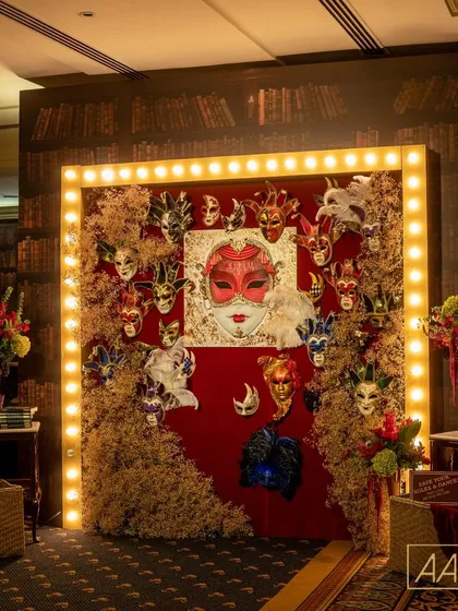 This grand entrance was designed to transport guests to a hidden world of mystery and glamour. The speakeasy masquerade theme came to life with a dramatic photo wall, combining vintage marquee lights with a rich texture of masks and dried foliage against a library-themed backdrop.
