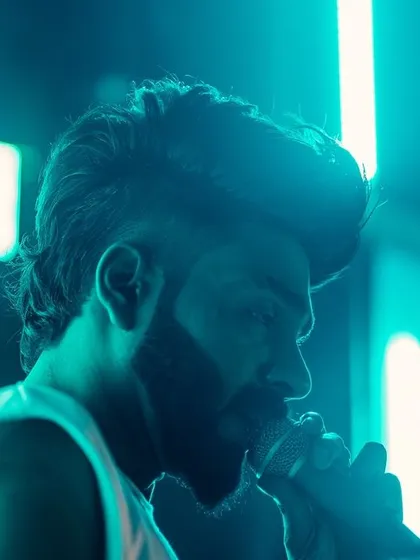 A close-up, atmospheric shot of me on the mic under cool blue lighting. The focus is on the connection between me, the music, and the crowd.