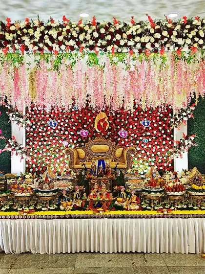 A breathtaking baby shower stage with hanging floral chandeliers and a backdrop of red and white flowers. The elaborate plate decoration in front completes the opulent and festive look.