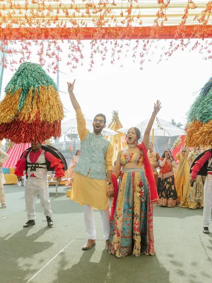 The couple raises their hands in celebration, surrounded by performers and guests. The energy is infectious.