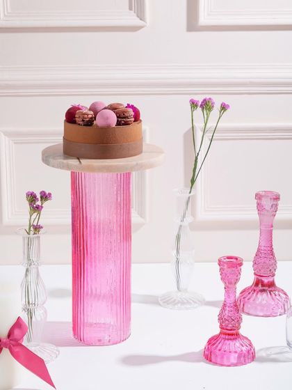 A beautiful cake topped with macarons and berries, standing tall on a pink pedestal. A cake a day keeps your sweet tooth at bay!