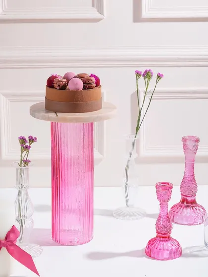 A beautiful cake topped with macarons and berries, standing tall on a pink pedestal. A cake a day keeps your sweet tooth at bay!