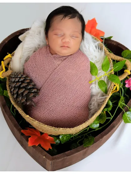 For this posed newborn session, I placed the baby in a heart-shaped basket, swaddled in a soft pink wrap. The setup is decorated with flowers and natural elements for a beautiful, rustic feel.