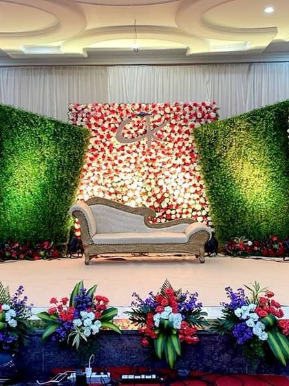 This reception stage uses a dynamic design of alternating floral and greenery panels. The angled panels create a sense of depth, while the bright red and white flowers stand out against the lush green backdrop.