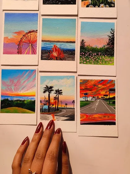 My hand reaching over a set of six vibrant landscape polaroids. Each one is a tiny, colorful world.