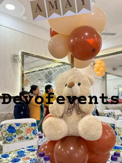 A cute and simple table centerpiece for a teddy bear party. A large, soft teddy bear sits on a base of balloons, adding a touch of the theme to every table.