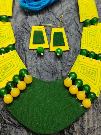 A bright and cheerful bib necklace in a vibrant yellow and green combination. The hand-drawn geometric patterns on the yellow fabric panels are complemented by green and yellow beads. This is a fun, colorful piece of statement jewelry perfect for adding a pop of color.