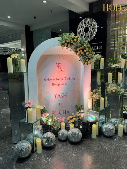 A glamorous welcome sign for Yash and Rucha's reception, set in a white arch and surrounded by disco balls, candles, and flowers for a party vibe.