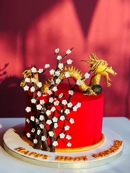 An elegant and powerful dragon cake. This custom design features a golden dragon wrapped around a vibrant red cake with delicate cherry blossoms, perfect for a unique birthday celebration.