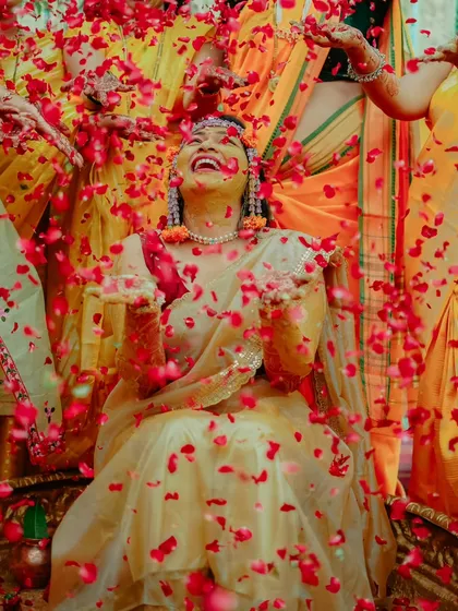 Pure, unadulterated joy during a Haldi ceremony. The air is filled with laughter and a shower of red rose petals, creating a memory of pure celebration.
