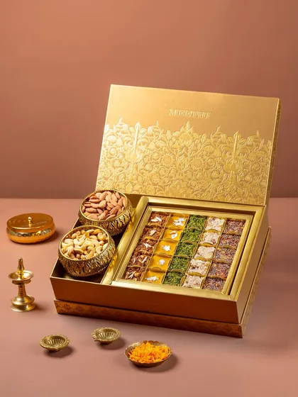 A luxury Indian sweet and dry fruit gift box for Meethi India, styled for a festive campaign. The composition uses traditional brass elements to create an opulent, celebratory feel, perfect for high-end product and packaging photography.