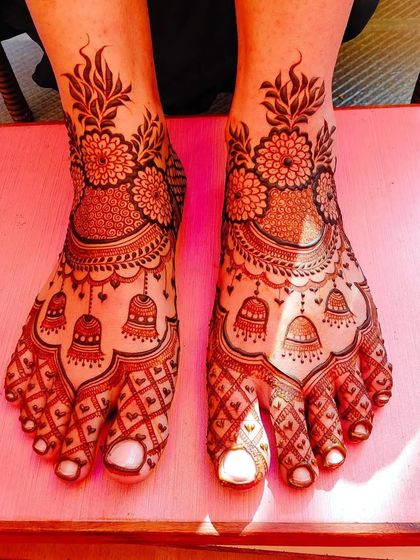 A beautiful foot mehandi with hanging jhumki (bell) motifs. The floral band at the top and the net pattern on the toes complete this festive design.