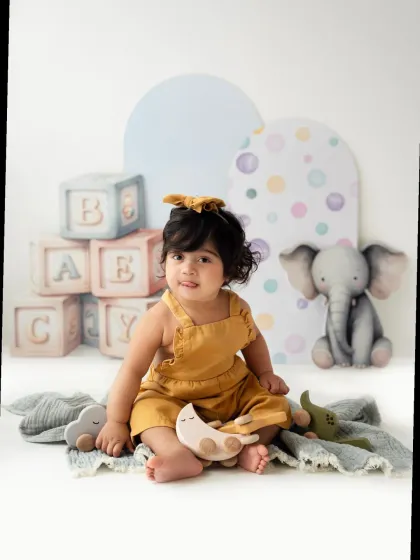 A sweet toddler girl in a yellow outfit surrounded by toys. Her happy expression is simply priceless.