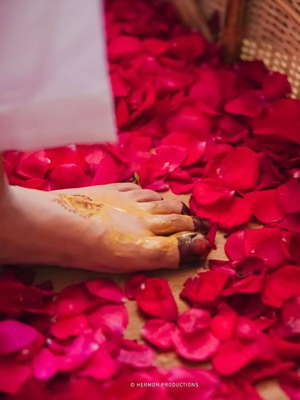 A symbolic image from a Haldi ceremony, with a foot stained with turmeric and henna stepping onto a bed of red rose petals.