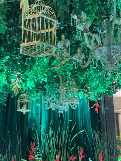 A detail from the "Jungle" theme entrance. Crystal chandeliers and vintage birdcages hang from a ceiling of lush green foliage, creating a magical and eclectic look.