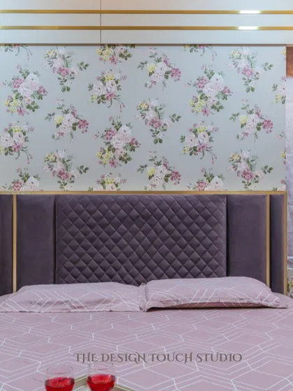 A close-up of the bed, showcasing the quilted purple headboard set against the delicate floral wallpaper. The combination of textures and patterns creates a rich and luxurious feel.