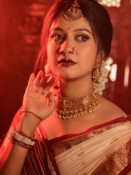 Portraits from a makeup shoot, showcasing a model in a classic red and cream saree. The images highlight the flawless makeup and traditional styling in a beautiful garden setting.