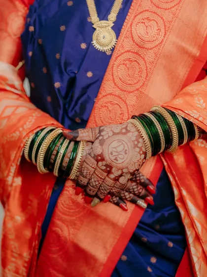 A detail shot focusing on the bride's hands, showcasing her intricate henna design with the couple's initials and her beautiful bangles. These details are an important part of the wedding story.