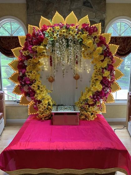 A grand sun-shaped backdrop with illuminated petals, framing a colorful floral arch. This is a bright and magnificent setup for a large celebration.