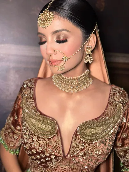 A close-up of this gorgeous bridal makeup. The focus is on the warm, bronze-toned eyeshadow, flawless skin, and traditional gold jewelry, creating a look of timeless beauty.