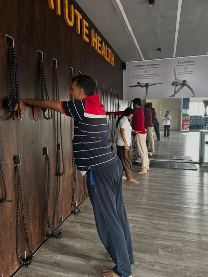 Students use the wall to perform a standing twist. This prop-assisted variation helps to deepen the spinal rotation and open the chest, improving flexibility and releasing tension in the back.