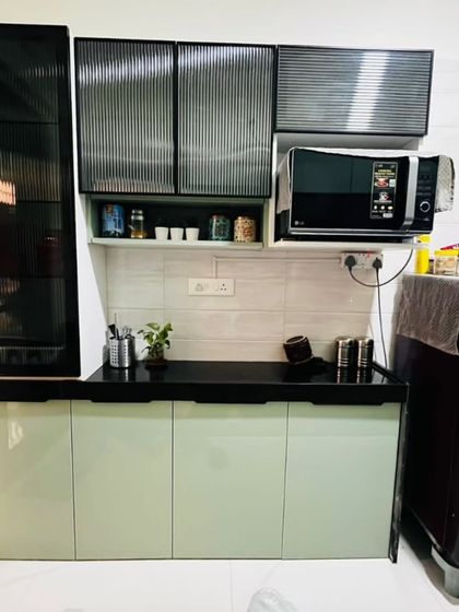 This kitchen combines soft mint-green cabinets with a bold black countertop and fluted glass shutters. The design includes a dedicated space for the microwave, keeping the counter free.