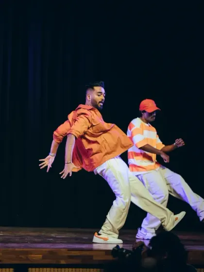 Dancers in bright orange outfits executing a synchronized move, showcasing the fun and vibrant energy of their performance.
