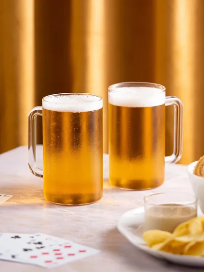 A warm, inviting shot of the beer mugs against a golden curtain. The lighting creates a cozy, evening ambiance perfect for enjoying a cold beer.