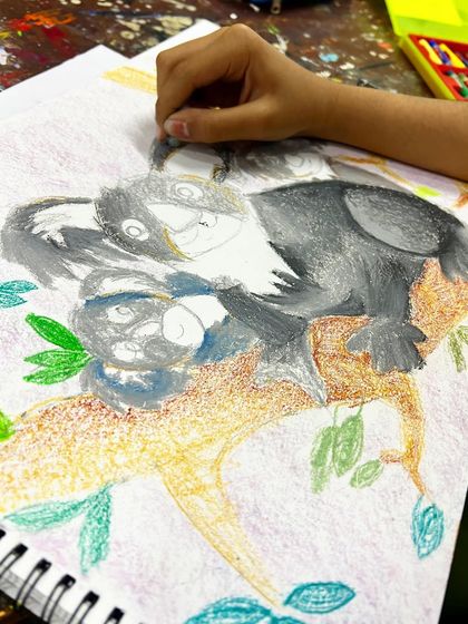 The coloring process begins. The student starts to add layers of grey with oil pastels, learning how to build up color and create texture for the koala's fur.