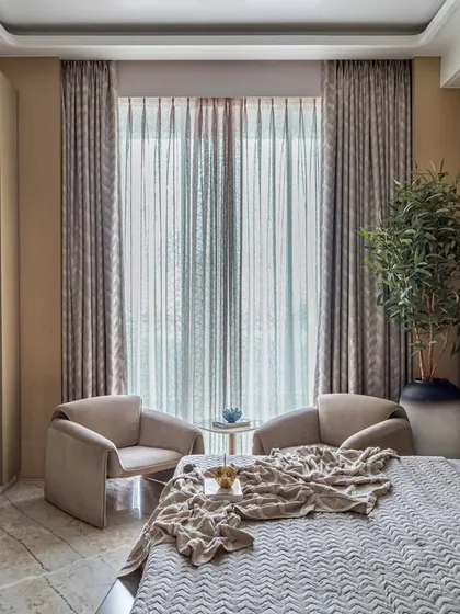 This bedroom exudes warmth and comfort with its soft, neutral palette and wooden wall paneling. A cozy two-chair seating nook by the window provides a perfect spot for morning coffee.