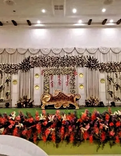This is an example of our classic and opulent floral stage design. The combination of a grand floral canopy, intricate side arrangements, and a regal golden chaise lounge creates a focal point of pure elegance.