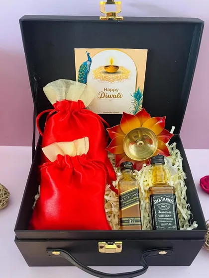 This black suitcase hamper for Diwali includes two miniature whiskeys, two satin potlis for treats, and a beautiful metal diya.