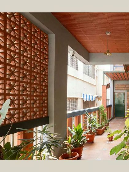 A beautiful terracotta jaali screen on a balcony provides privacy and ventilation while creating artistic shadow patterns. The space is filled with potted plants, enhancing the green character.