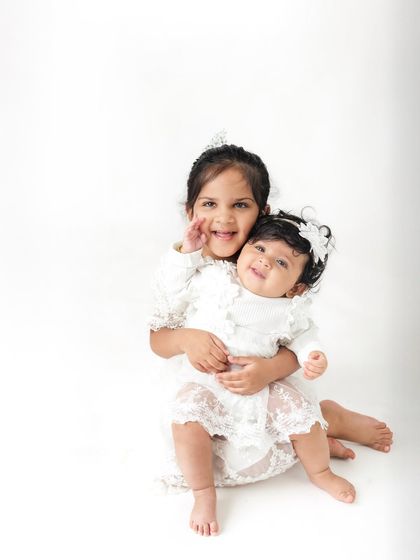 Halfway to one. This simple and classic six-month milestone portrait on a clean white background highlights the beautiful bond between two sisters.