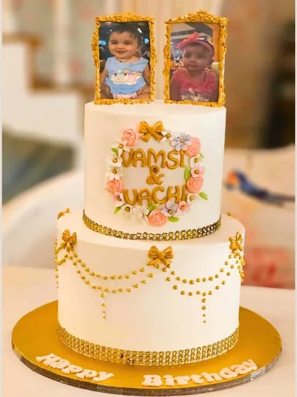 A heartwarming two-tier cake with edible photo frames, a floral wreath, and delicate gold details, celebrating two young children.